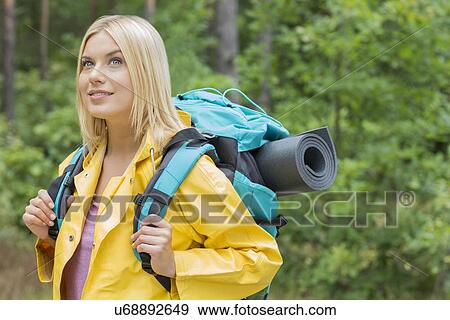 Stock Photo - Smiling female backpacker in raincoat looking away at forest. Fotosearch