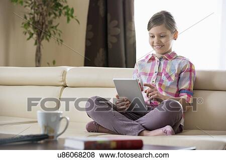 Smiling girl using digital tablet on sofa at home View Large Photo Image Stock Photo - Smiling girl using digital tablet on sofa at home. Fotosearch
