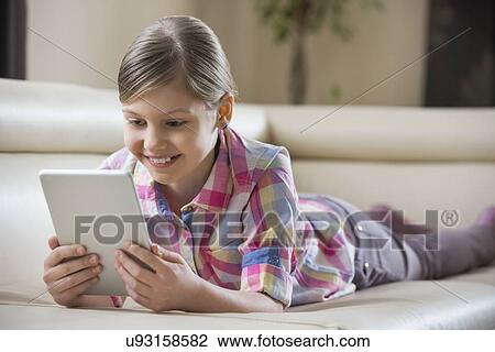 Smiling girl using tablet PC while lying on sofa at home View Large Photo Image Stock Image - Smiling girl using tablet PC while lying on sofa at home. Fotosearch