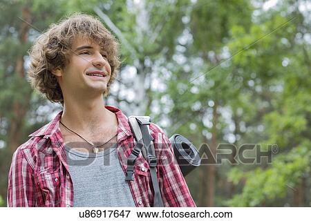 Stock Photo - Smiling male hiker looking away in forest. Fotosearch