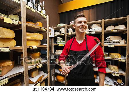 Smiling male salesperson holding knife in cheese store View Large Photo Image Picture - Smiling male salesperson holding knife in cheese store. Fotosearch