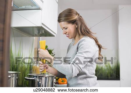 Stock Image - Smiling woman preparing spaghetti in kitchen. Fotosearch
