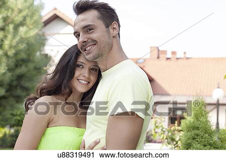 Stock Image - Smiling young couple embracing outdoors. Fotosearch