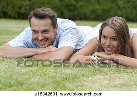 Stock Image - Smiling young couple lying on grass. Fotosearch