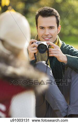 Smiling young man photographing woman in park View Large Photo Image Stock Image - Smiling young man photographing woman in park. Fotosearch
