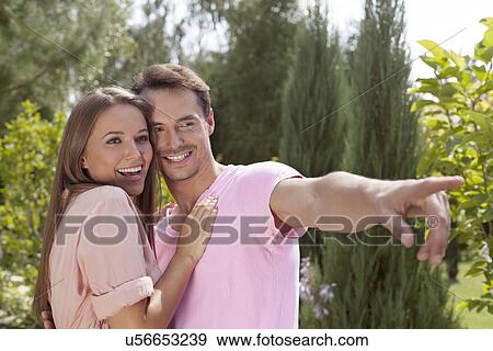 Stock Photo - Smiling young man showing something to woman in park. Fotosearch