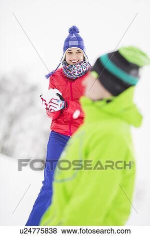 Stock Photo - Smiling young woman having snowball fight with male friend. Fotosearch
