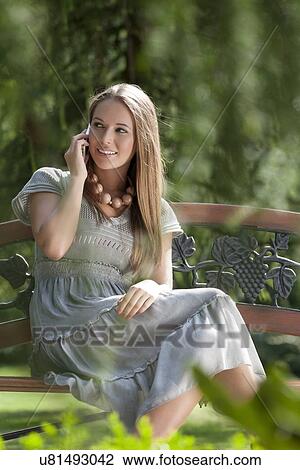 Smiling young woman using mobile phone on park bench View Large Photo Image Stock Image - Smiling young woman using mobile phone on park bench. Fotosearch