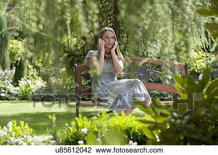 Tensed young woman using cell phone on bench in park View Large Photo Image Stock Image - Tensed young woman using cell phone on bench in park. Fotosearch