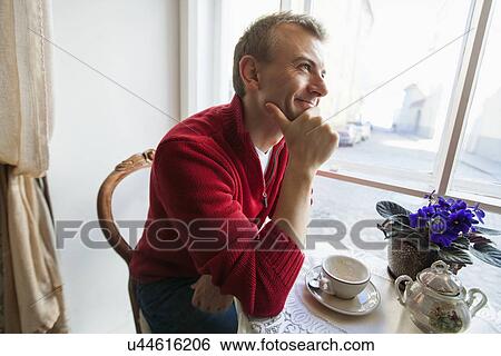 Thoughtful mid adult man sitting at table in cafe View Large Photo Image Stock Photograph - Thoughtful mid adult man sitting at table in cafe. Fotosearch