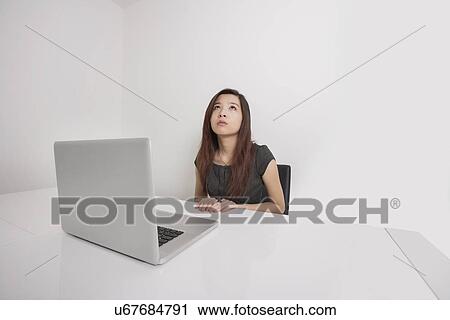 Thoughtful young businesswoman looking up with laptop at office desk View Large Photo Image Stock Image - Thoughtful young businesswoman looking up with laptop at office desk. Fotosearch