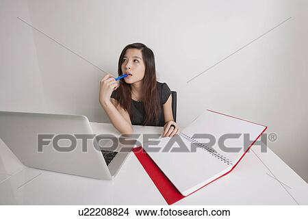 Picture - Thoughtful young businesswoman with diary and laptop at office desk. Fotosearch