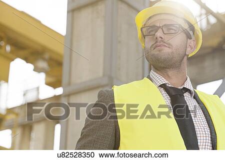 Thoughtful young male architect in protective wear at construction site View Large Photo Image Stock Image - Thoughtful young male architect in protective wear at construction site. Fotosearch