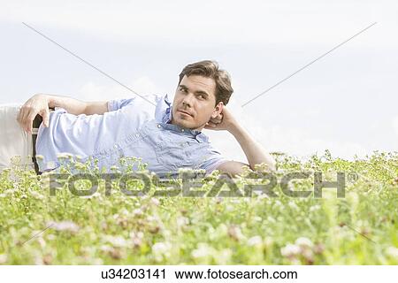 Thoughtful young man lying on grass against sky View Large Photo Image Stock Image - Thoughtful young man lying on grass against sky. Fotosearch