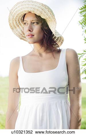 Stock Image - Thoughtful young woman in sundress and hat looking away in park. Fotosearch