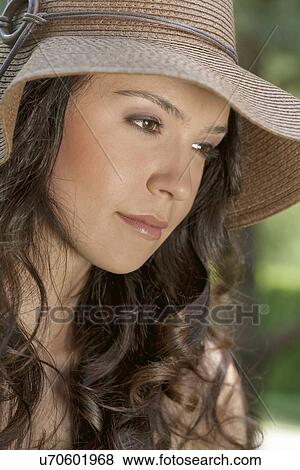 Stock Photo - Thoughtful young woman wearing sunhat in park. Fotosearch