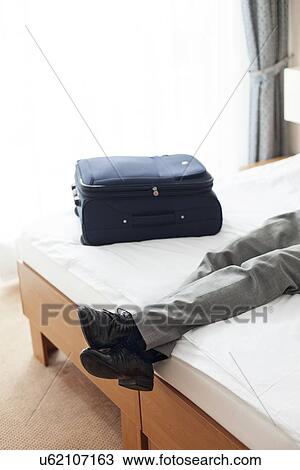 Tired young man lying on bed in hotel room View Large Photo Image Stock Image - Tired young man lying on bed in hotel room. Fotosearch