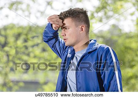 Tired young man wiping sweat after jogging at park View Large Photo Image Stock Image - Tired young man wiping sweat after jogging at park. Fotosearch