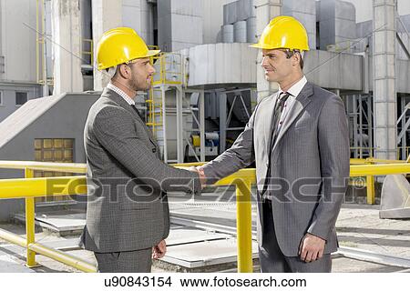 Two male architects shaking hands at construction site View Large Photo Image Picture - Two male architects shaking hands at construction site. Fotosearch