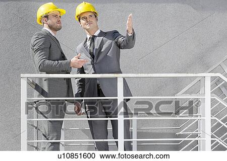 Two young businessmen in hard hats discussing on stairway View Large Photo Image Stock Image - Two young businessmen in hard hats discussing on stairway. Fotosearch