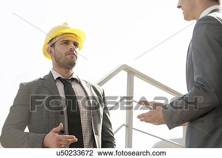 Stock Image - Two young male engineers discussing on stairway against clear sky. Fotosearch