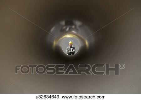 Stock Photo - View of confident male architect through large pipe at construction site. Fotosearch