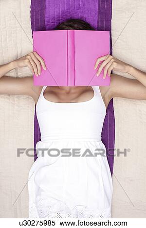Stock Photography - Woman covering face with book while lying on picnic blanket. Fotosearch