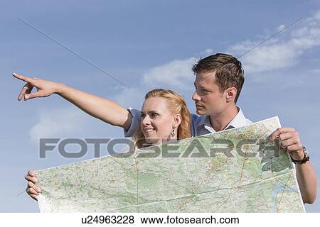 Woman holding map while man pointing away against sky View Large Photo Image Stock Photo - Woman holding map while man pointing away against sky. Fotosearch