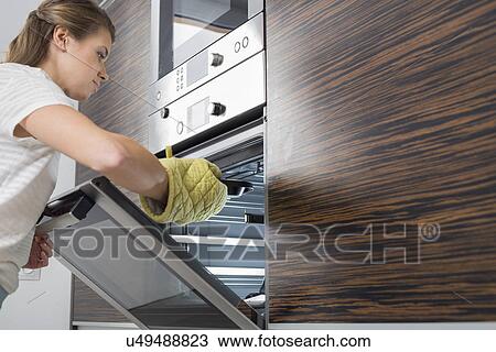 Woman placing dish in oven View Large Photo Image Stock Image - Woman placing dish in oven. Fotosearch