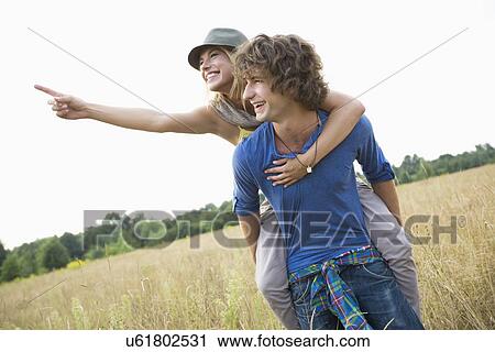 Woman showing something while enjoying piggyback ride on man in field View Large Photo Image Stock Image - Woman showing something while enjoying piggyback ride on man in field. Fotosearch
