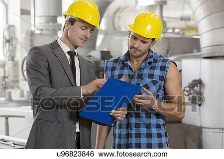 Stock Photograph - Worker with manager discussing over clipboard in industry. Fotosearch