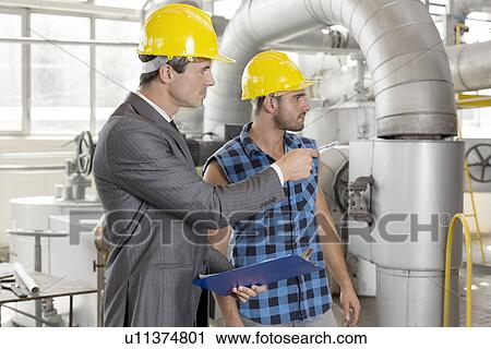 Stock Image - Worker with supervisor inspecting industrial area. Fotosearch