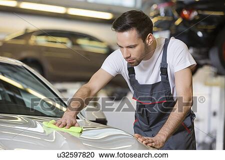 Stock Image - Young automobile mechanic cleaning car in repair shop. Fotosearch