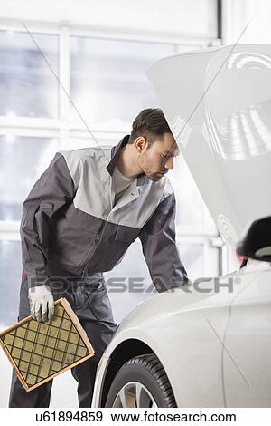 Stock Photo - Young automobile mechanic examining car in automobile shop. Fotosearch
