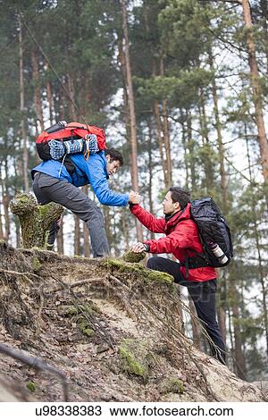 Young backpacker assisting friend while hiking in forest View Large Photo Image Stock Image - Young backpacker assisting friend while hiking in forest. Fotosearch