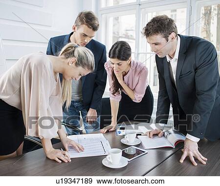 Stock Photo - Young business people brainstorming at conference table in office. Fotosearch