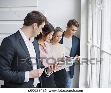 Stock Photography - Young business people working by window in office. Fotosearch