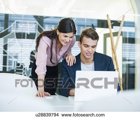 Young businessman and businesswoman using laptop at table in office View Large Photo Image Picture - Young businessman and businesswoman using laptop at table in office. Fotosearch