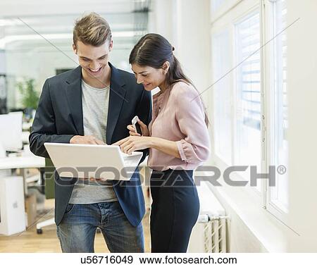 Stock Photo - Young businessman and businesswoman using laptop in office. Fotosearch