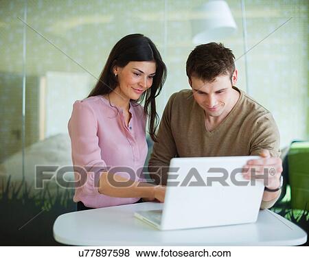 Stock Photo - Young businessman and businesswoman using laptop at office table. Fotosearch