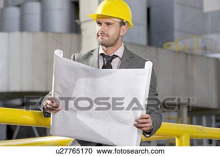 Young businessman holding blueprint while looking away at construction site View Large Photo Image Stock Image - Young businessman holding blueprint while looking away at construction site. Fotosearch