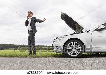 Young businessman using cell phone by broken-down car at countryside View Large Photo Image Picture - Young businessman using cell phone by broken-down car at countryside. Fotosearch
