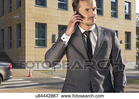 Young businessman using cell phone against office building View Large Photo Image Stock Photo - Young businessman using cell phone against office building. Fotosearch