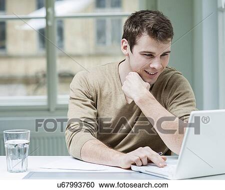 Young businessman using laptop at desk in office View Large Photo Image Stock Image - Young businessman using laptop at desk in office. Fotosearch