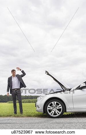 Young businessman waving for help by broken down car at countryside View Large Photo Image Stock Photo - Young businessman waving for help by broken down car at countryside. Fotosearch