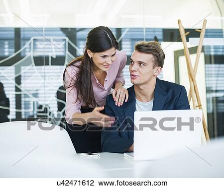 Young businessman with female colleague discussing over laptop at table in office View Large Photo Image Stock Image - Young businessman with female colleague discussing over laptop at table in office. Fotosearch