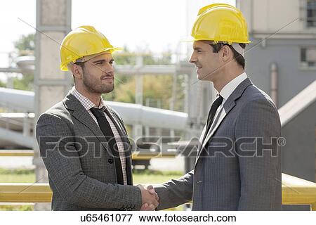 Young businessmen in hard hats shaking hands at construction site View Large Photo Image Stock Photo - Young businessmen in hard hats shaking hands at construction site. Fotosearch