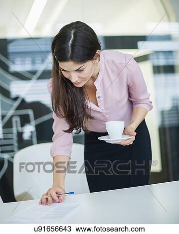 Young businesswoman reading document while holding coffee in office View Large Photo Image Stock Image - Young businesswoman reading document while holding coffee in office. Fotosearch