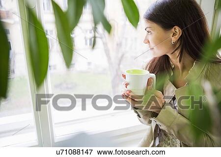 Young businesswoman with coffee cup looking through window at office View Large Photo Image Stock Photo - Young businesswoman with coffee cup looking through window at office. Fotosearch