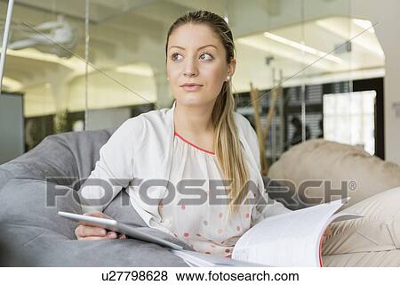 Young businesswoman with tablet PC and book looking away in office View Large Photo Image Stock Photo - Young businesswoman with tablet PC and book looking away in office. Fotosearch
